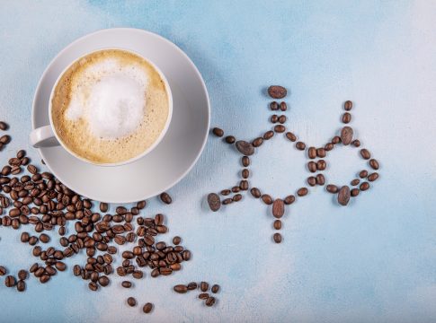 a cup of coffee with caffeine molecule created by coffee beans. Chemical formula of Caffeine with roasted coffee spill out of cup on blue wooden background.
