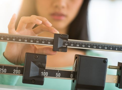 Midsection of mid adult Asian woman adjusting balance weight scale Midsection of mid adult Asian woman adjusting balance weight scale