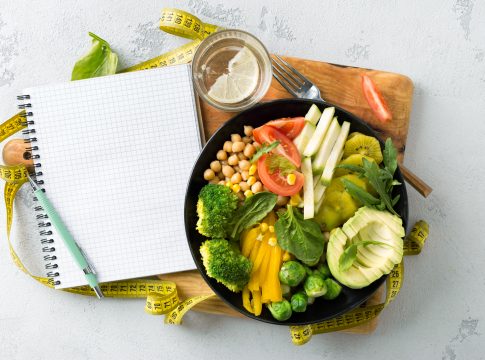Vegan healthy balanced diet concept. Vegetarian buddha bowl with blank notebook and measuring tape. hickpeas, broccoli, pepper, tomato, spinach, arugula and avocado in plate on white background. Top view