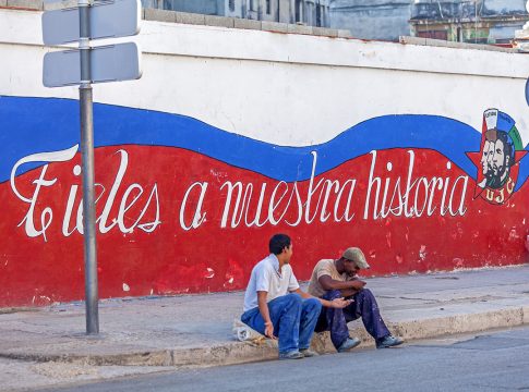Havana, Cuba - April 2, 2012: Two cuban teenagers sitting near propaganda graffiti Havana, Cuba - April 2, 2012: Two cuban teenagers sitting near propaganda graffiti