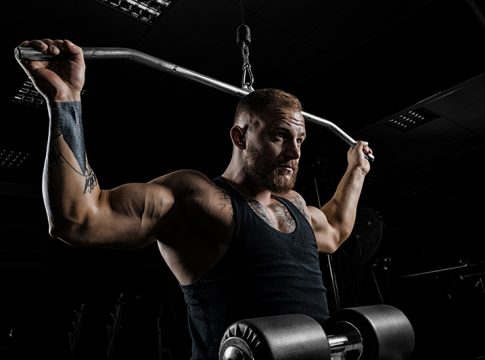 Professional athlete performs an exercise in the gym. Pulls the bar to the back of the head. Exercise for development of back muscles