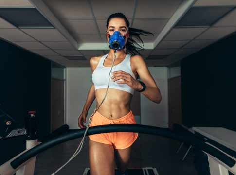 Sportswoman with mask running on treadmill. Female athlete in sports science lab measuring her performance and oxygen consumption. Sportswoman with mask running on treadmill. Female athlete in sports science lab measuring her performance and oxygen consumption.