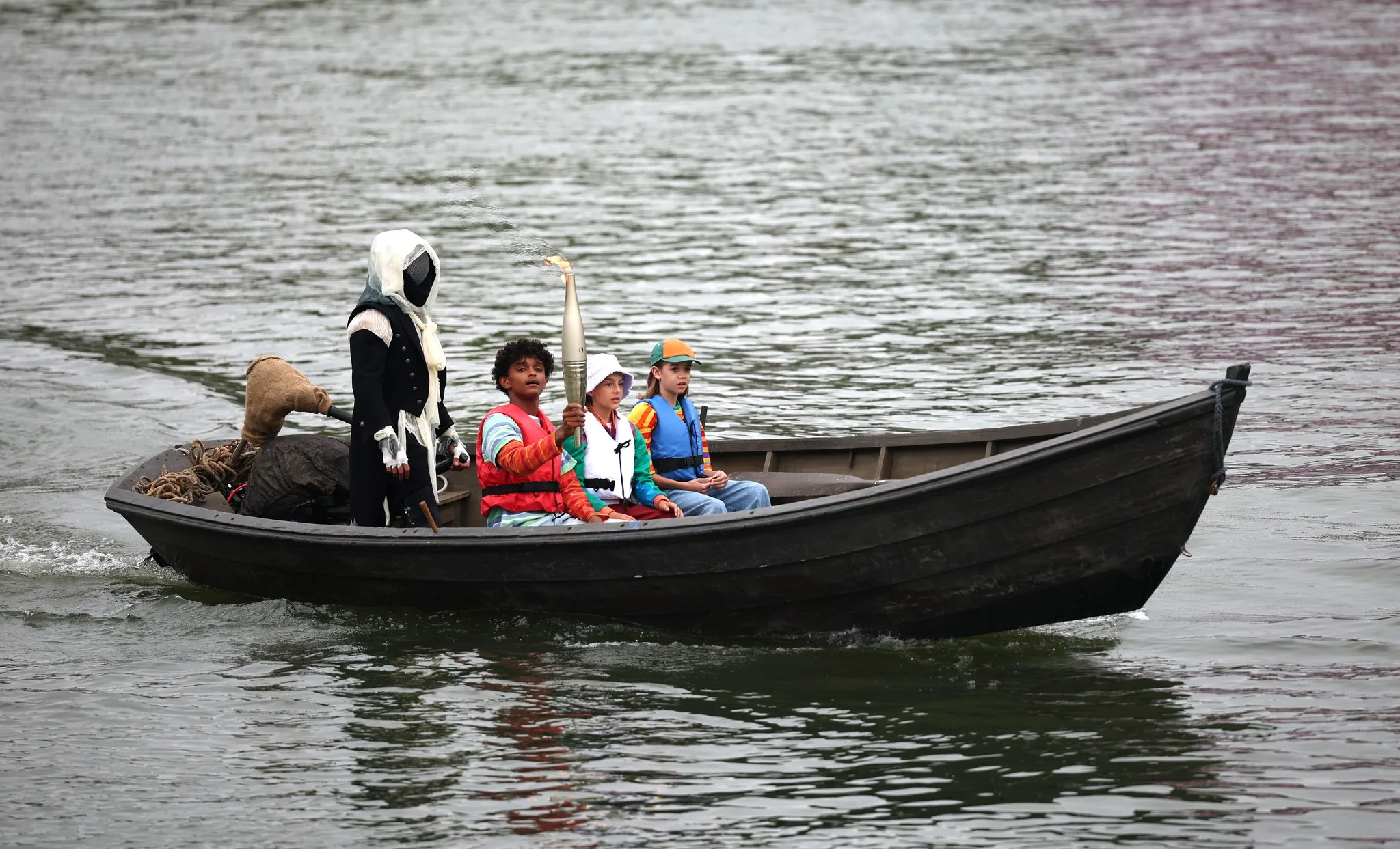 Enquanto os barcos das delegações deslizavam pelas águas do Sena, a Tocha Olímpica passou a circular pela cidade levada por um personagem misterioso vestido com roupas antigas e sem mostrar o rosto, inspirado no "Assassin´s Creed", um jogo eletrônico que se passa em castelos medievais.